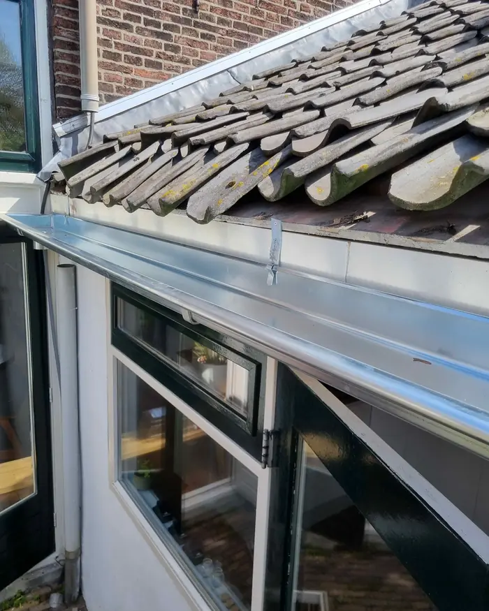 Nieuwe zinken dakgoot tegen een pannendak